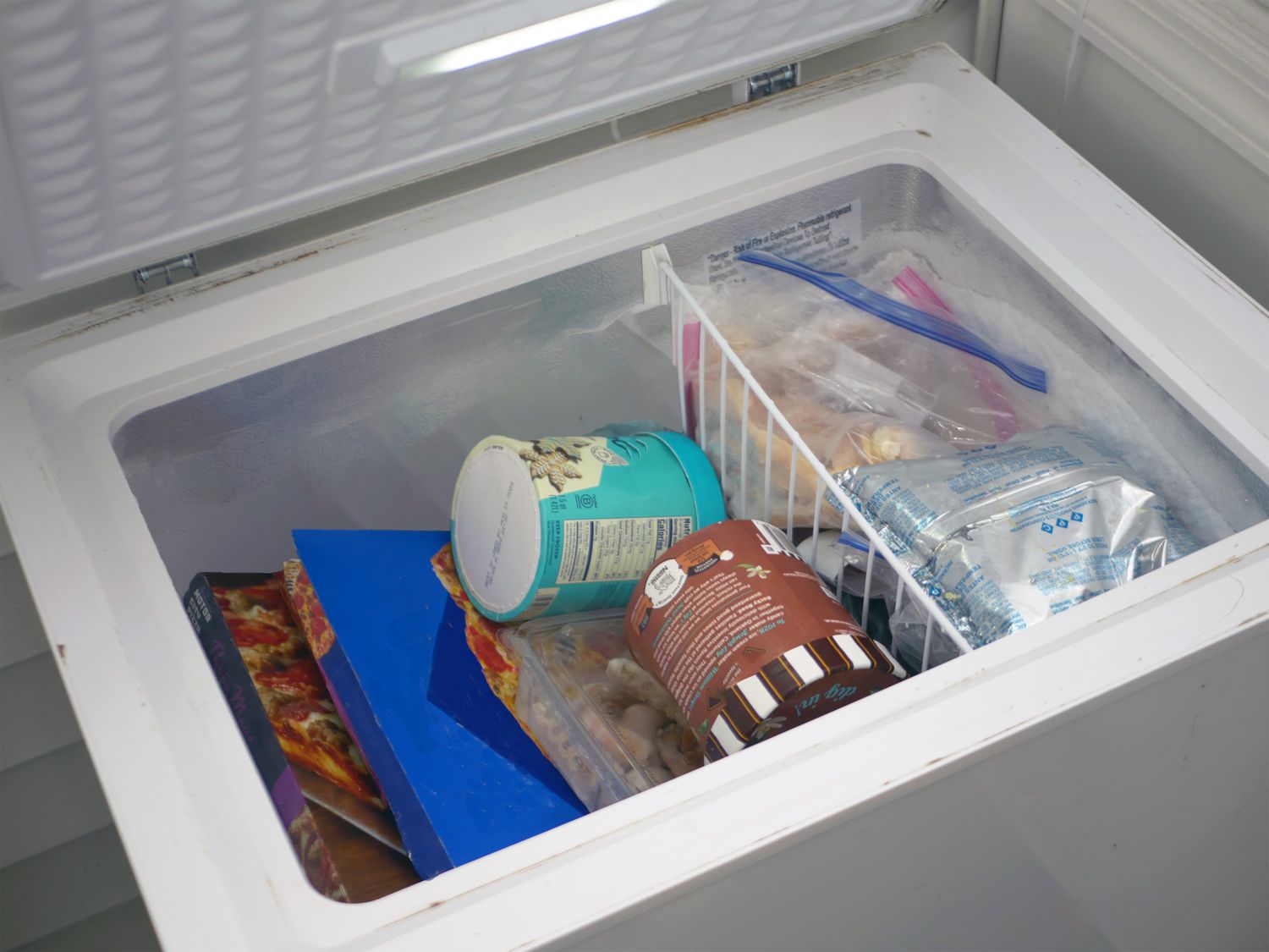 A chest freezer placed in a basement laundry area with enough clearance to open the lid fully.