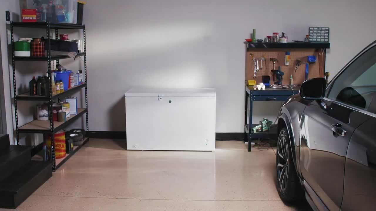 A closed white chest freezer against a wall in a typical home garage with a power outlet nearby.