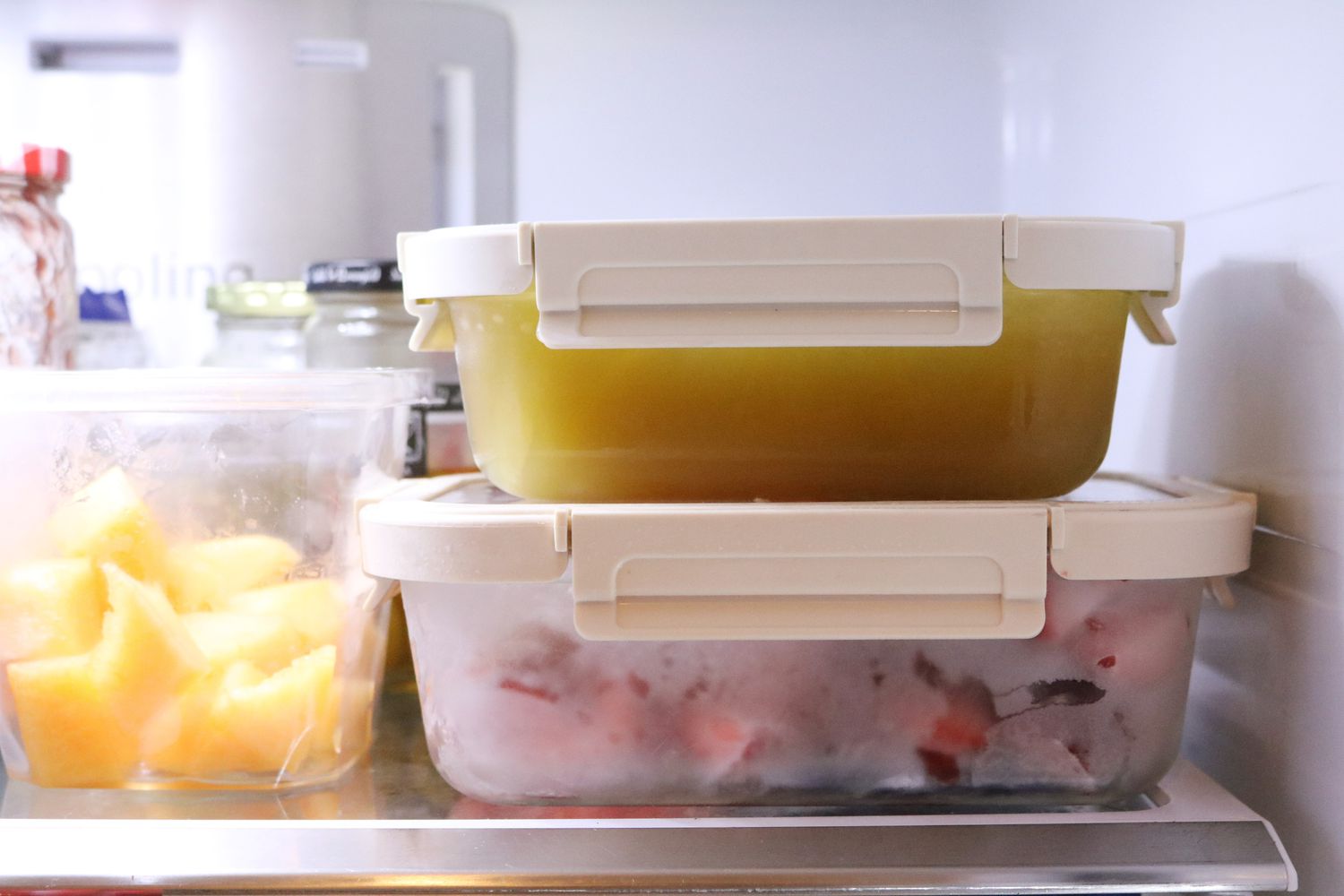 Stacked meal prep containers filled with frozen soups and stews arranged neatly inside a freezer drawer.